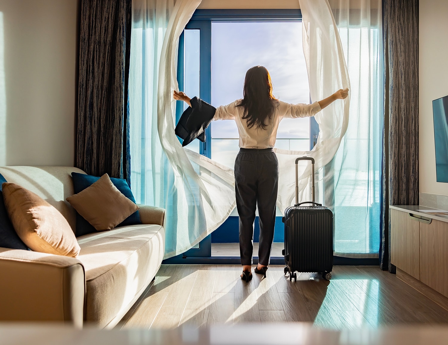 Woman opening curtains in hotel room.
