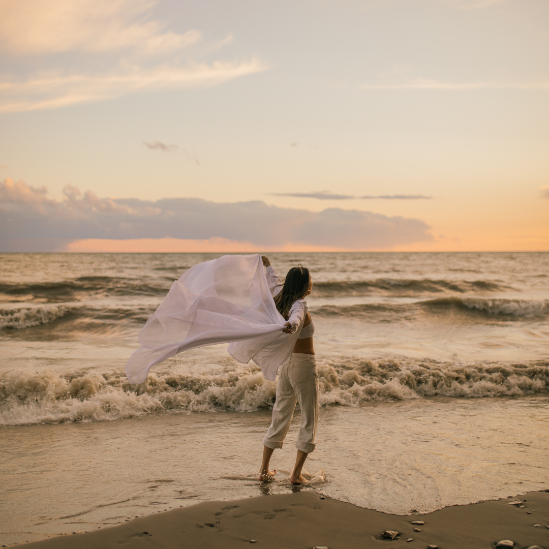 Woman in flowing fabric at sunset beach.