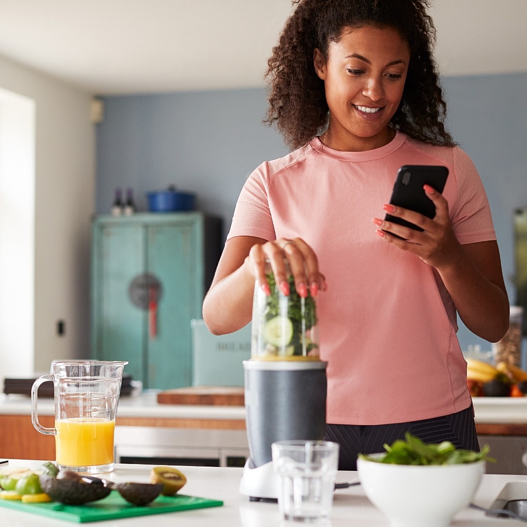 Woman using blender while checking her phone