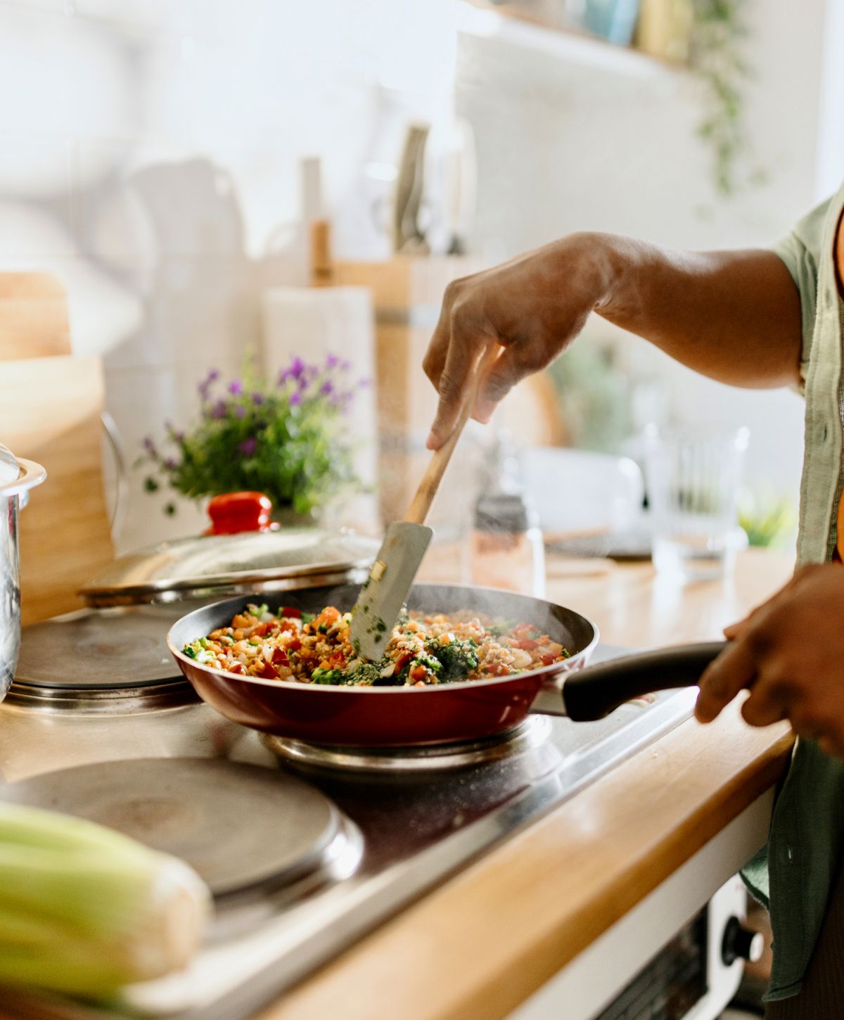Person cooking colorful vegetables in kitchen skillet.