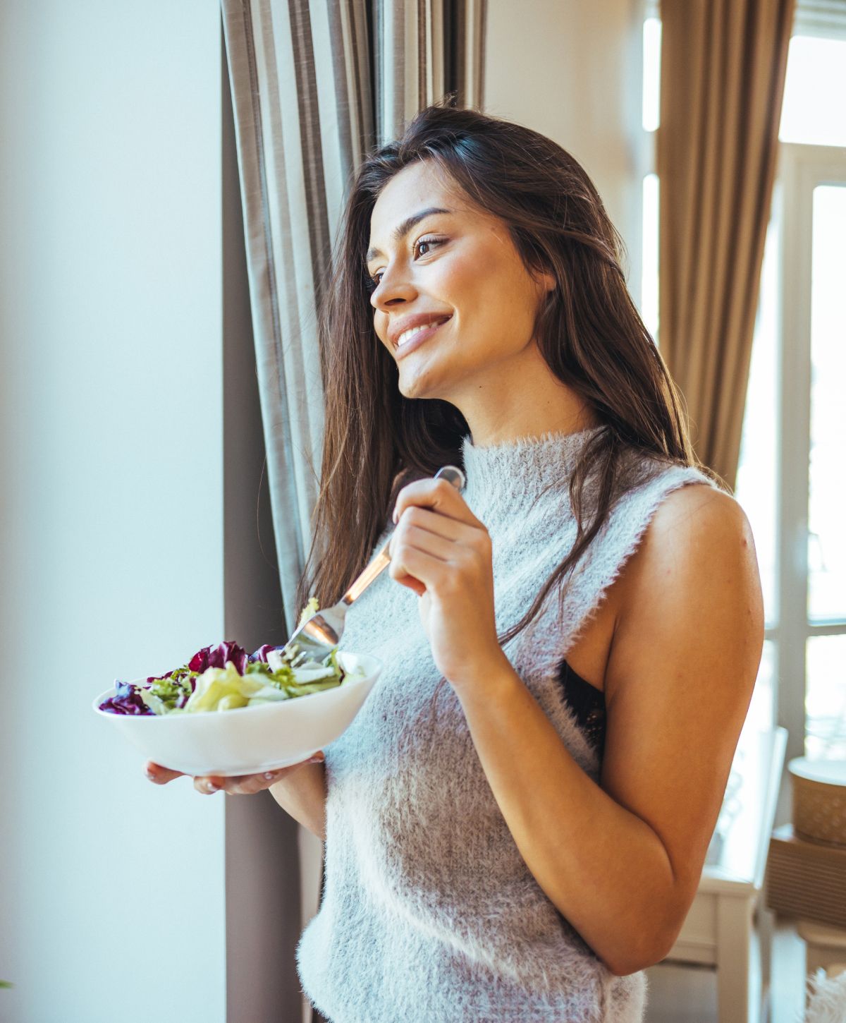 Woman enjoying a healthy salad by the window.