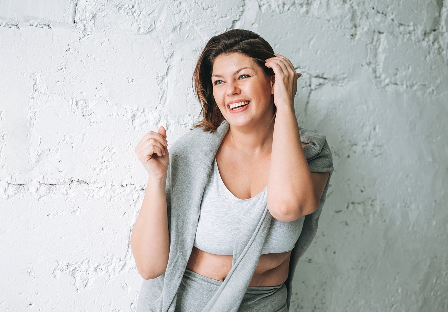 Smiling woman in gray outfit against white wall.