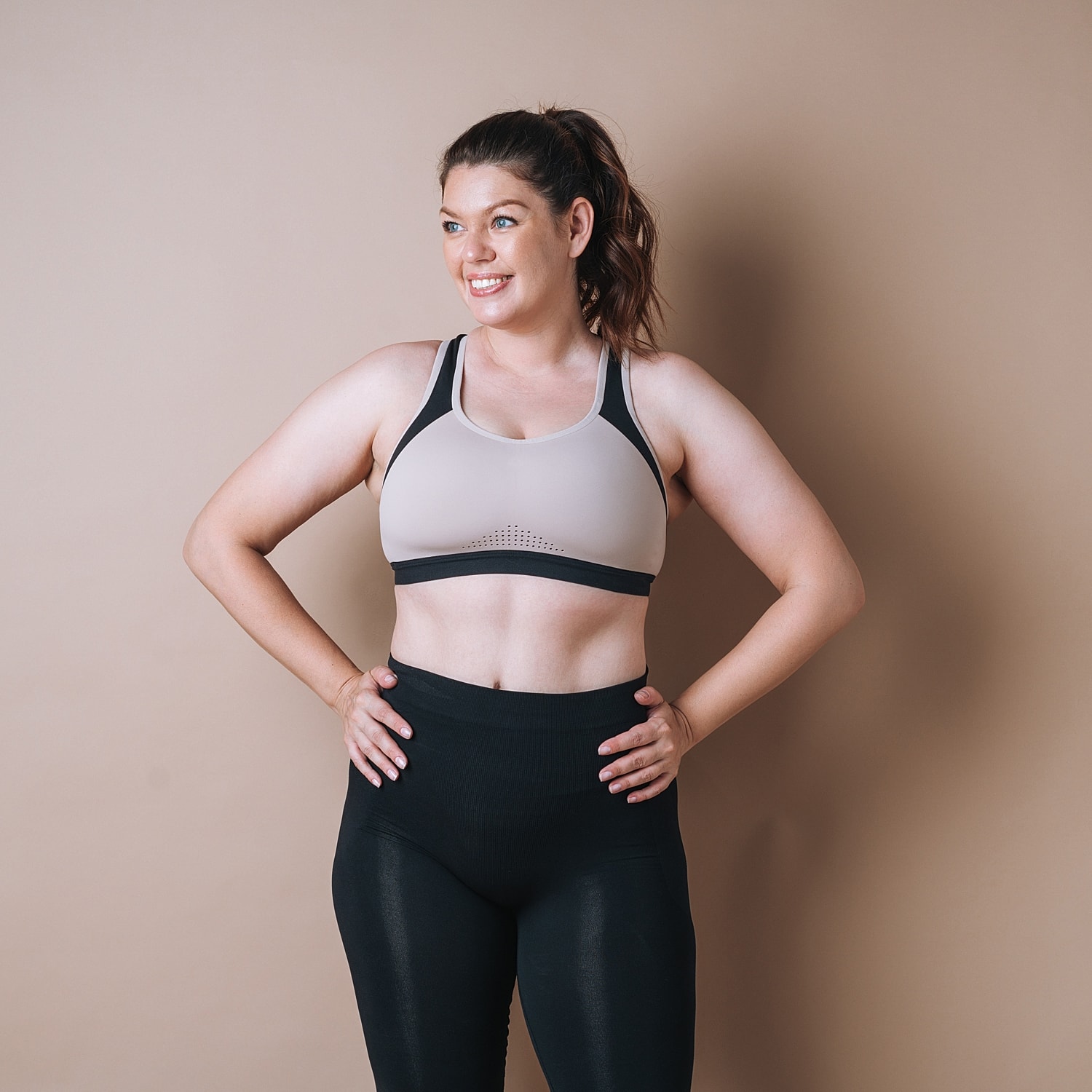 Smiling woman in athletic wear against beige backdrop.