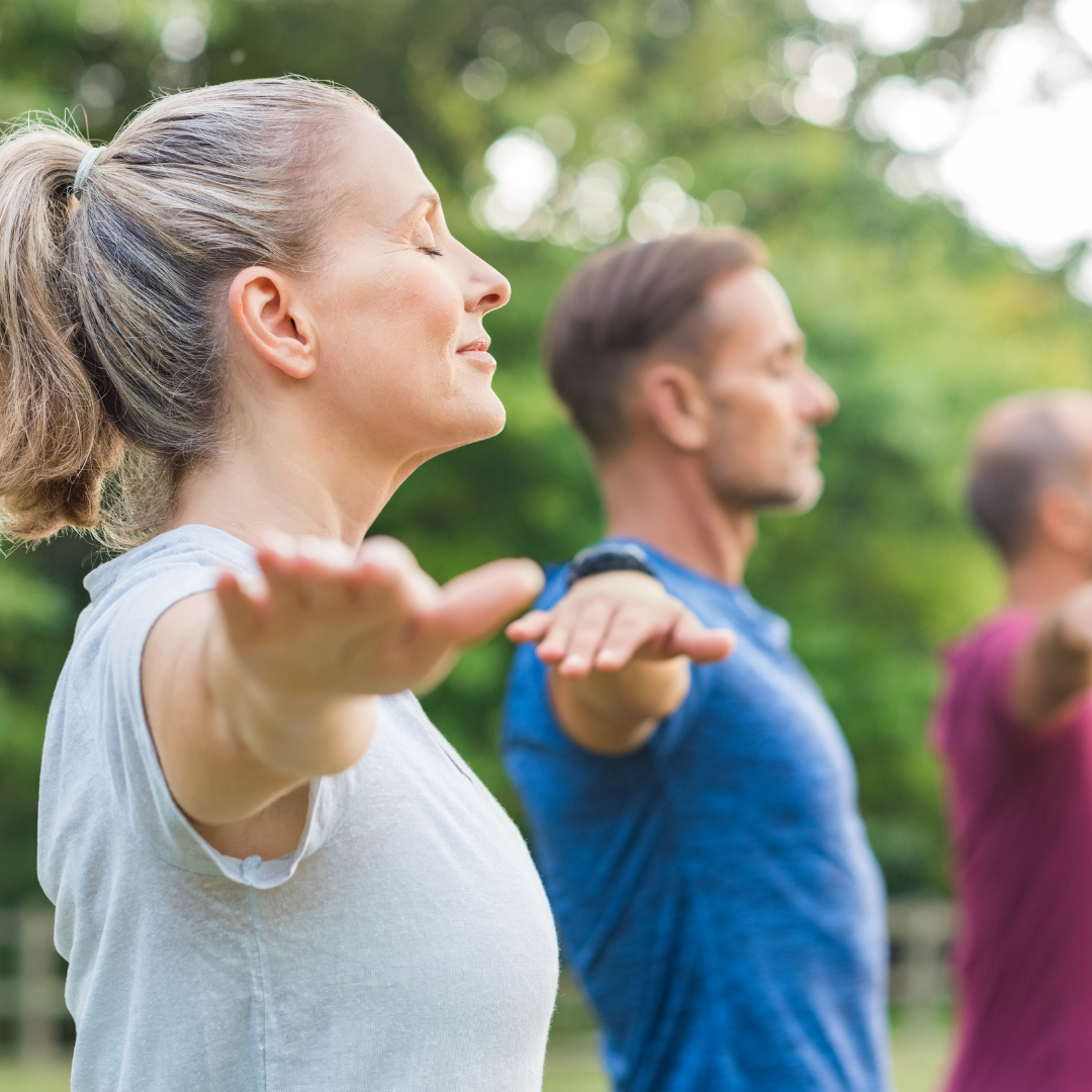 Group practicing yoga outdoors with arms extended.