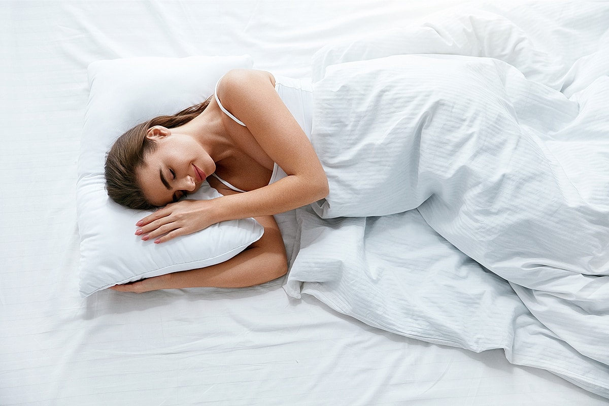 Woman peacefully sleeping on a white bed.